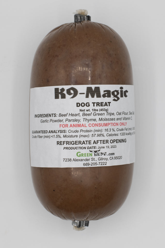 A rolled up treat labeled 'K9 Magic Dog Treat' with visible ingredients such as beef heart, beef green tripe, oat flour, sea salt, and parsley.