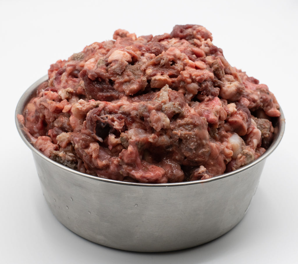 Raw ground tripe and organ meats piled in a stainless steel bowl on a white background. To be fed as pet food. 