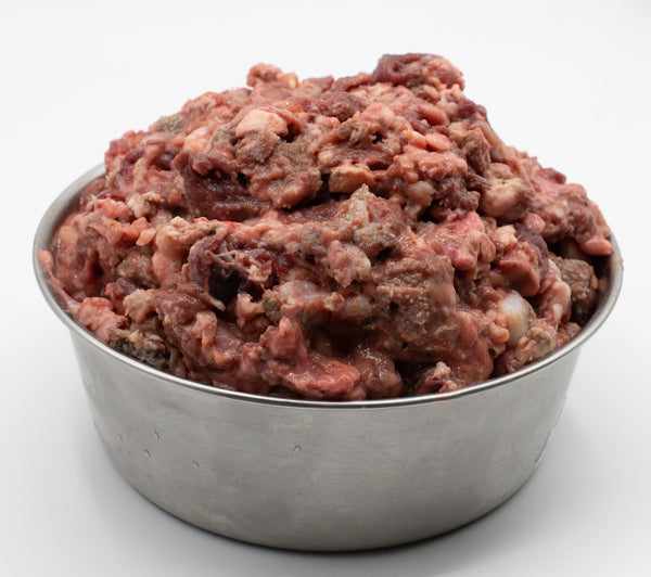 Raw ground tripe and organ meats piled in a stainless steel bowl on a white background. To be fed as pet food. 